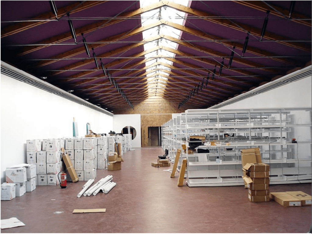 Interior view of a spacious art storage area with white shelves and various boxes, displaying a setup for an exhibition or archive.